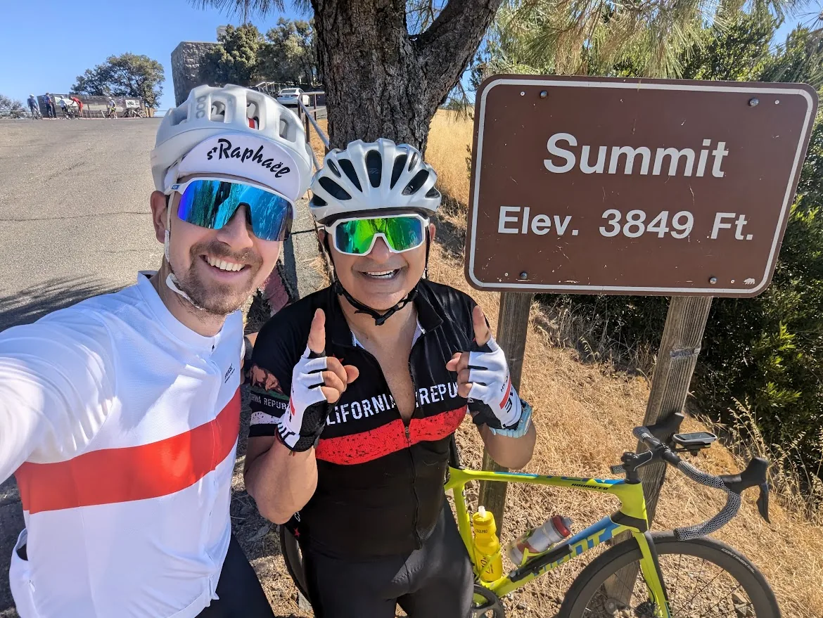 Two cyclists giving thumbs up at the Mt. Diablo Summit sign, elevation 3,849 feet